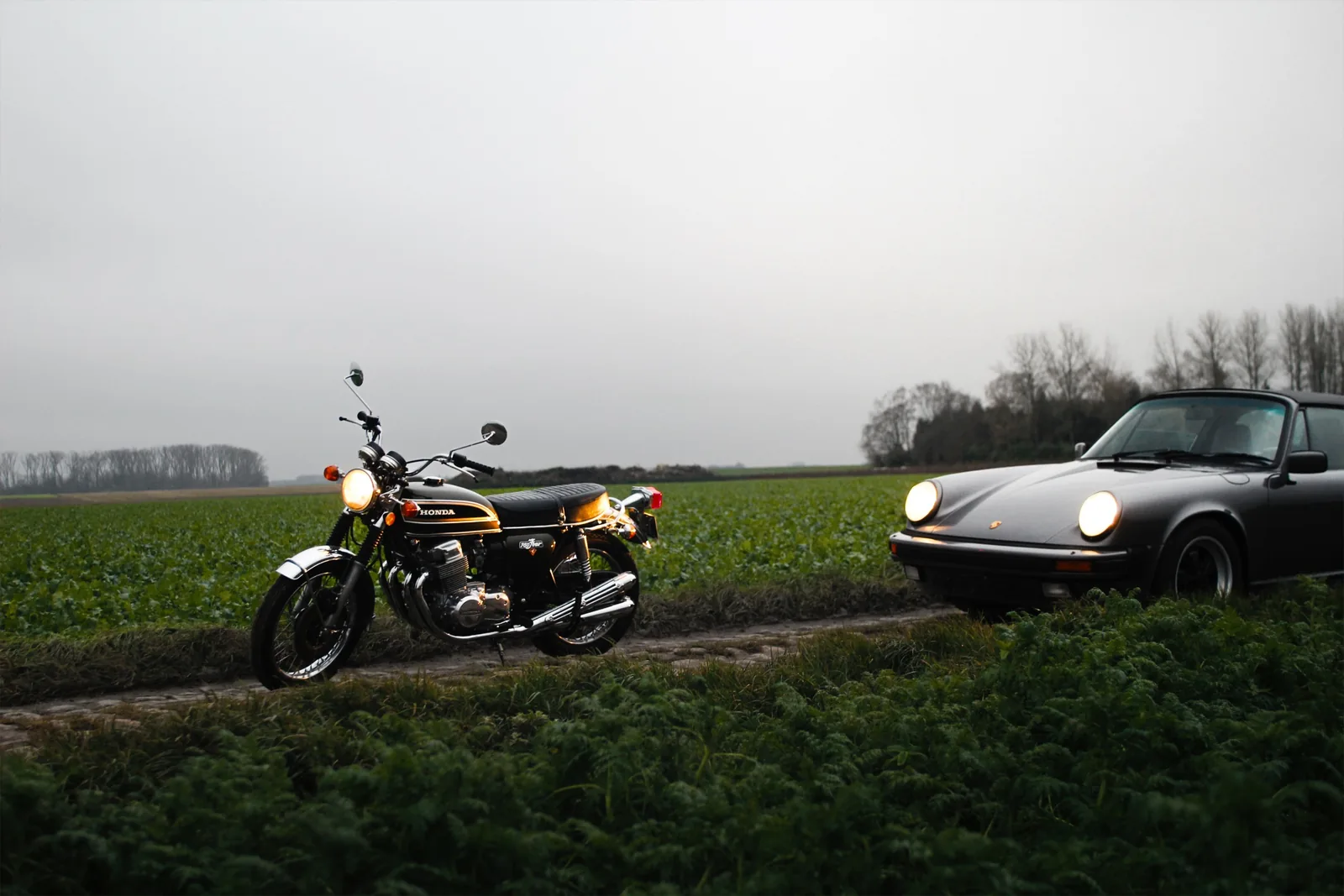 Une Honda CB750 et une Porsche 911 côte à côte dans un champ au crépuscule