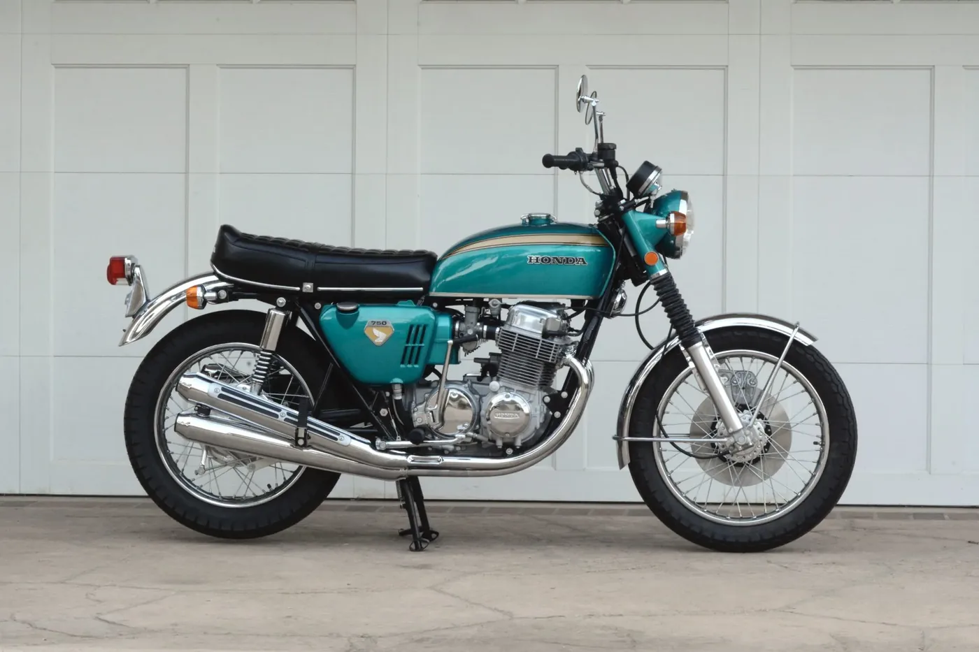 Honda CB750 turquoise restaurée devant un mur blanc